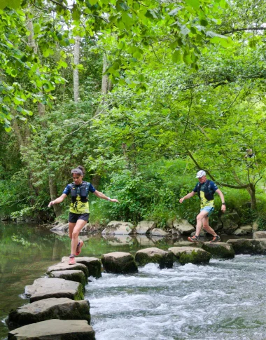 Deux trailers courent sur des pas japonais au cœur du site naturel de Saulges, en Mayenne, progressant de pierre en pierre dans un décor sauvage et verdoyant.