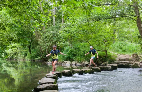 Deux trailers courent sur des pas japonais au cœur du site naturel de Saulges, en Mayenne, progressant de pierre en pierre dans un décor sauvage et verdoyant.